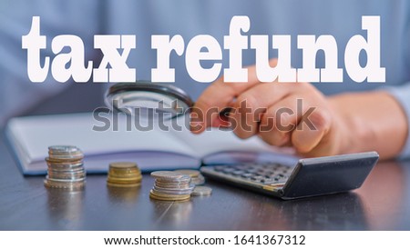 text "tax refund" ,  blurred picture in the background - magnifier in hand and stack of coins lies on a dark office desk next to a calculator, organizer,  tax refund concept