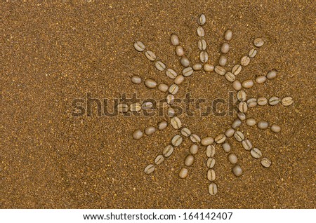 A sun with rays made of coffee beans on a background of ground coffee