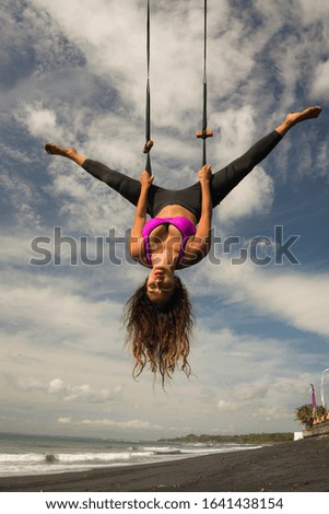 aero yoga beach workout - young attractive and athletic woman practicing aerial yoga exercise training acrobatic  body postures on blue sky over sea in Bali island healthy lifestyle concept

