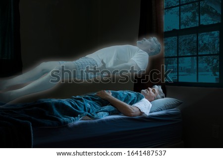Glowing spirit or angel coming out of a dead man who has died in his sleep as it floats above him ascending into heaven as moonlight shines on the poor gentleman. Royalty-Free Stock Photo #1641487537
