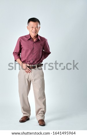An old asian man wear red shirt and beige pants stand on studio white  background. Isolated picture of happiness asian old man.