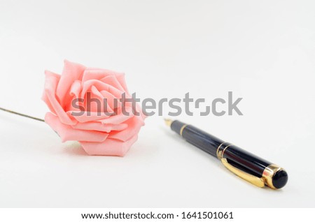 Black pen and pink rose on white background