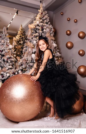 fashion photo of beautiful cute girl with dark hair with dark hair in elegant dress posing in decorated interior with Christmas tree