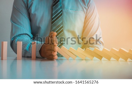 Businessman stopping domino effect with his hand, strategy and successful intervention concept for business.