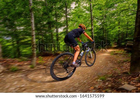 Motion blur picture of cycling woman riding on bike in autumn mountains forest landscape. Woman ride MTB flow trail track. Outdoor sport activity.