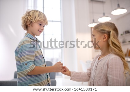 At home. Boy and girl clenching little fingers, looking at each other and smiling