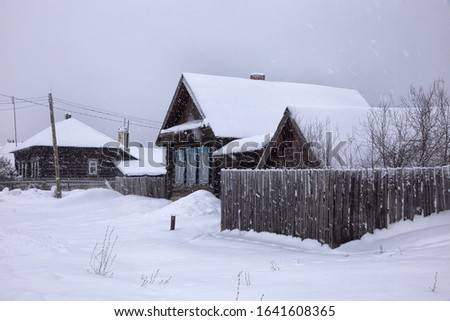 Village street in winter in snowfall gloomy day