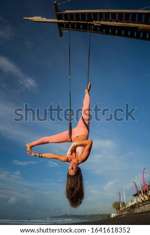 aerial yoga beach workout - young attractive and healthy woman practicing aero-yoga training balance body and mind control hanging from ropes above the sea isolated on beautiful blue sky