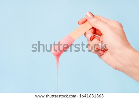 liquid pink pearl wax or sugar paste for depilation drains from the stick on blue background. The concept of depilation, waxing, sugaring smooth skin without hair, banner, copy space Royalty-Free Stock Photo #1641631363