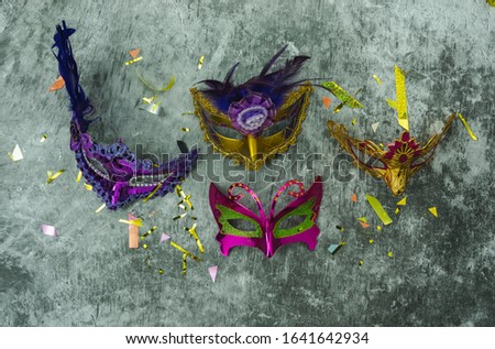 Table top view aerial image of beautiful colorful carnival festival background.Flat lay accessory object the several mask & decor confetti on modern grey cement at home office desk studio.copy space.