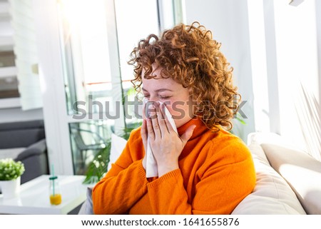Sick desperate woman has flu. Rhinitis, cold, sickness, allergy concept. Pretty sick woman has runnning nose, rubs nose with handkerchief. Sneezing female. Brunette sneezing in a tissue