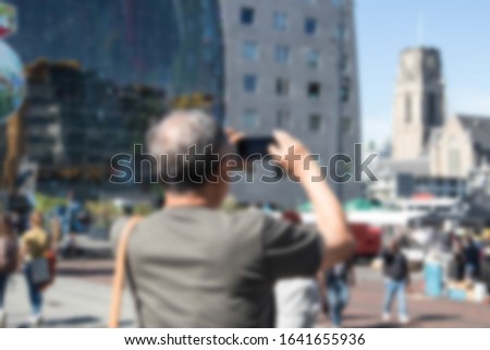 Abstract blurred rear view of male tourist taking a sightseeing photo on his mobile phone