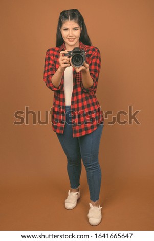 Young beautiful Asian woman wearing red checkered shirt against brown background