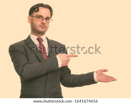Studio shot of young businessman pointing finger while showing something
