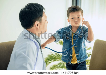 The image of a cute little boy goes to the doctor and is teasing the doctor using a stethoscope to listen to the doctor's heart.