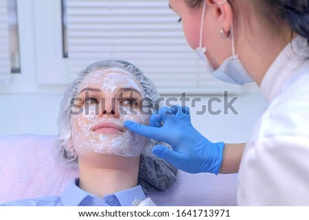 Cosmetologist is applying cream with anesthesia on patient's face skin before biorevitalization procedure. Woman in beauty clinic with doctor beautician preparing to treatment using numbing cream.