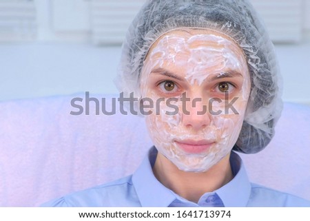 Woman with anesthetic cream on face skin before biorevitalization, portrait closeup. Beauty procedure in cosmetology clinic. Young woman is waiting for anesthesia to take effect looking at camera.