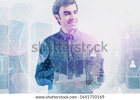 Smiling young businessman working with laptop in city with double exposure of blurry social network interface. Concept of job search and communication. Toned image