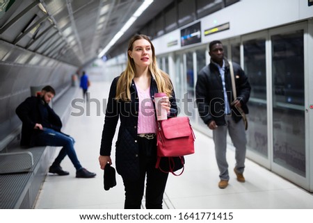 Portrait of young female passenger waiting for subway train, walking at modern underground station