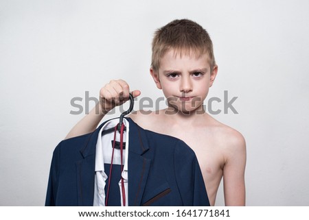 Unhappy child boy holds a business suit, school uniform. Young business boy is going to work.