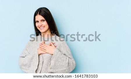 Young caucasian woman isolated on blue background has friendly expression, pressing palm to chest. Love concept.