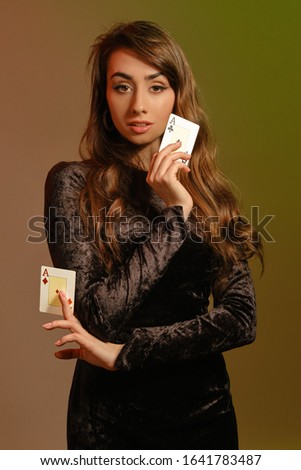 Brunette maiden in black velvet dress and jewelry showing two aces, posing against colorful studio background. Gambling, poker, casino. Close-up.