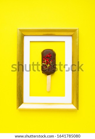 Brownie cake in form of popsicle in golden frame on yellow background. Dessert as  Art
