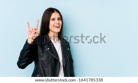 Young caucasian woman isolated on blue background showing a horns gesture as a revolution concept.