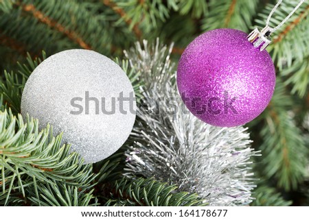 Two christmas balls hangind on a green tree.