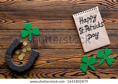 Composition for St. Patrick's Day.
Decorating paper with green clover or shamrocks, leprechaun hat and horseshoe.
Dark wooden background top view,flat lay, mockup