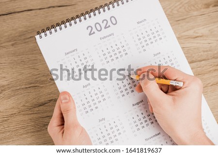 Cropped view of man noting date with pencil on calendar on wooden background