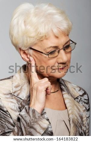 An old woman touching her face, worried. Over grey background.
