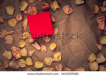 Red gift box with pink flower petals on crumpled kraft paper. Flat lay. Copy space on the box, for the brand. Suitable for layout. Vignetting.