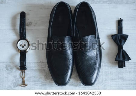 Men's black leather shoes, a bow-tie and a stylish watch close-up on a white parquet background. Morning and preparation of the groom. Gentleman's set. Photography, concept.