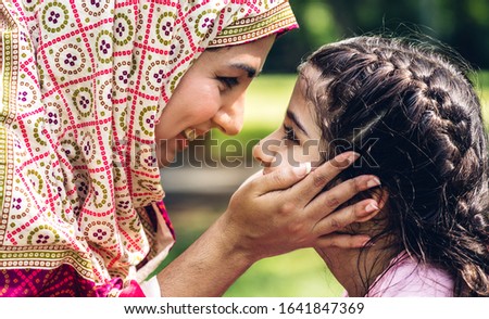 Portrait of happy lovely family arabic muslim mother and little muslim girls child with hijab dress smiling and having fun kissing together in summer park