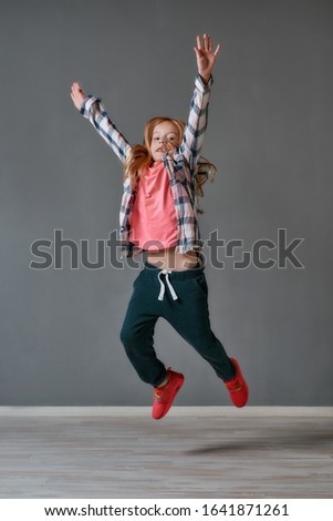 In motion. Portrait of a cute and excited little girl in casual clothes jumping in the dance studio. Looking at camera. Choreography class. Happy children