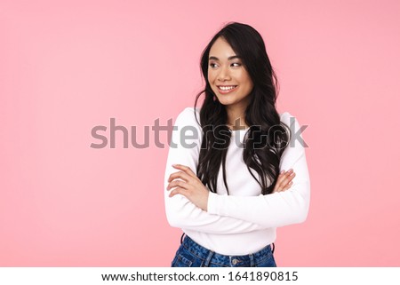 Image of young brunette asian woman in casual clothes standing with arms crossed and looking aside isolated over pink background