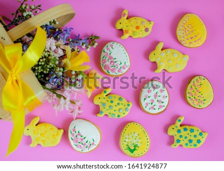 Flat lay of spring picture with basket of spring flowers and easter ginger cookies in the shape of easter eggs and easter bunnies on a pink background. Easter cookies eggs and rabbits in the icing