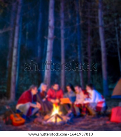 Blurred colorful abstract conceptual scene with tourist people sit around bonfire near camping tent in forest at night. Group of student at outdoor fire. Travel activity and vacation weekend concept