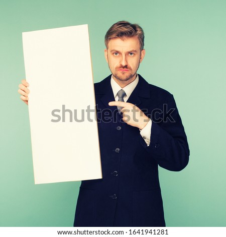 Happy smiling young business man points finger blank signboard, on blue background. toned