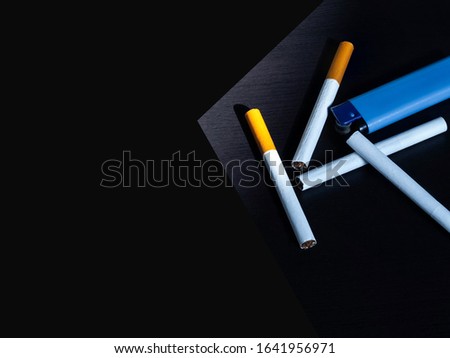 Cigarettes and one blue lighter placed on the black floor in a dark area.  