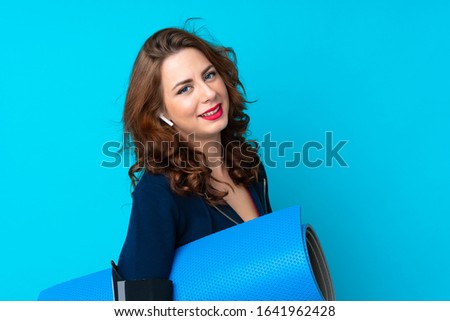 Young sport woman over isolated blue background with a mat and smiling
