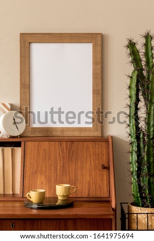 Stylish retro composition of workspace with vintage wooden cabinet, cup of coffee, design pot with cacti, mock up picture frame and elegant personal accessories Vintage concpet of home decor. Template