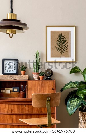 Stylish retro composition of home office  interior with vintage wooden cabinet, chair, plants, clock, pendant lamp and elegant accessories. Gold mock up poster frame. Retro home decor Template