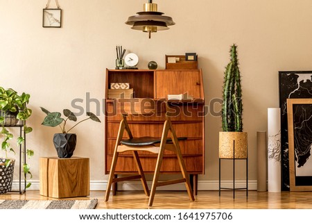 Retro interior design of living room with wooden vintage bureau, design chair, plants, cacti, maps, brown pendant lamp and elegant personal accessories. Stylish home decor. Beige wall. Template. 