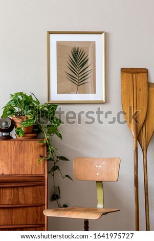 Stylish and vintage interior design of living room with wooden retro commode and chair, plants, paddle and elegant personal accessories. Mock up poster frame on the wall. Template. Home decor.