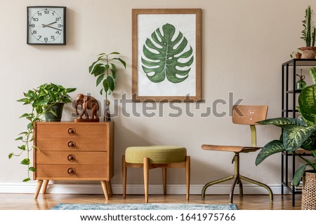 Vintage interior design of living room with design retro furnitures, plants, shelf, black clock and brown poster mock up frame on the beige wall. Stylish home decor. Template. 