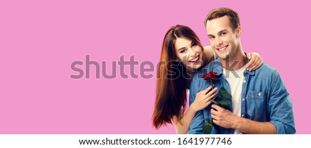 Love, relationship, dating, flirting, romantic concept - portrait picture of happy couple with flower, looking at camera. Over rose pink color background. Copy space for some text.