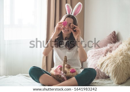 Teenager girl with Easter ears and a wicker Easter basket closes her eyes with eggs on a bed in a living room. Emotions. Easter concept