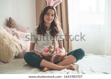 Teenager girl with Easter ears and a wicker Easter basket on a bed in a living room. Emotions. Easter concept